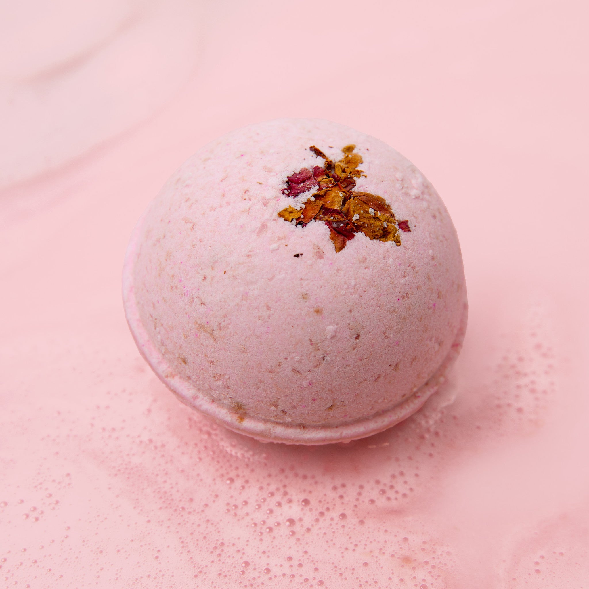 Soakshow CBD Bath Bomb in Vanilla Rose with real rose petals on top, resting on a pink background.