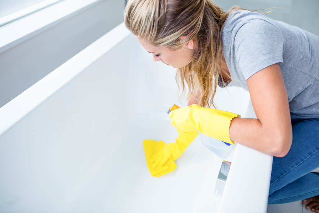Woman wears protective gloves while cleaning a bath tub