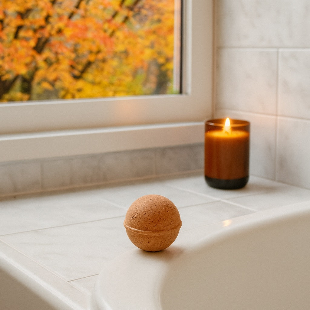 Soakshow CBD Bath Bomb in Vanilla Sandalwood next to a candle by a window with autumn trees.